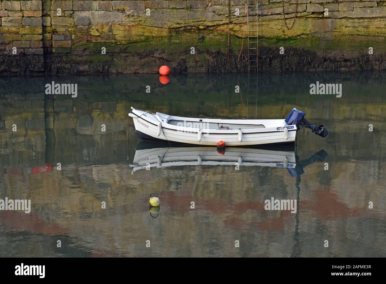 Solitario piccola barca a Dysart Harbour in Fife, riflette ancora in acqua con la parete del porto in background. Foto Stock