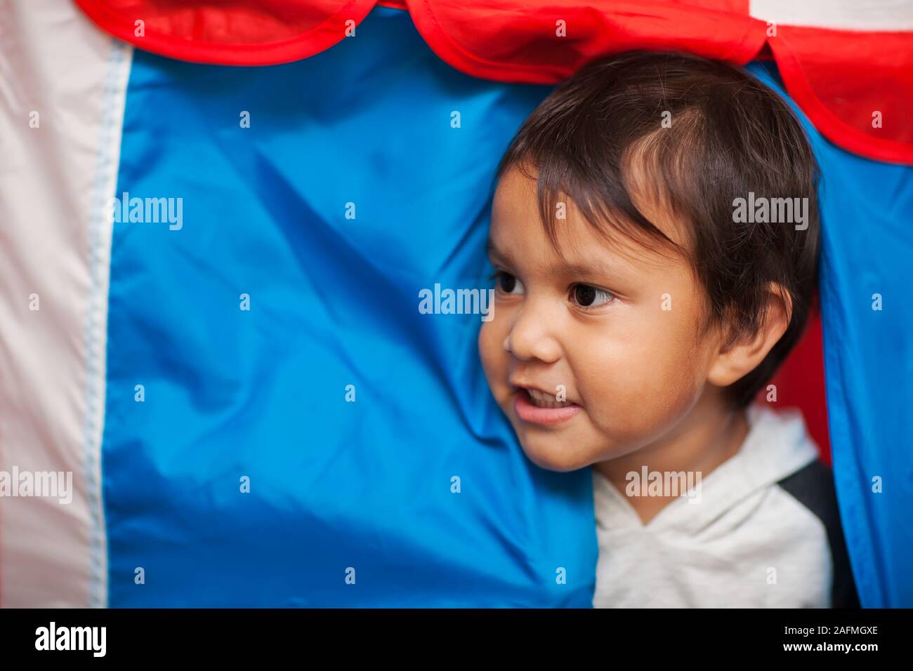 Il volto di un bambino con capelli wispy, tra l'ingresso ad un gioco tenda che ha colori rosso, bianco e blu. Foto Stock