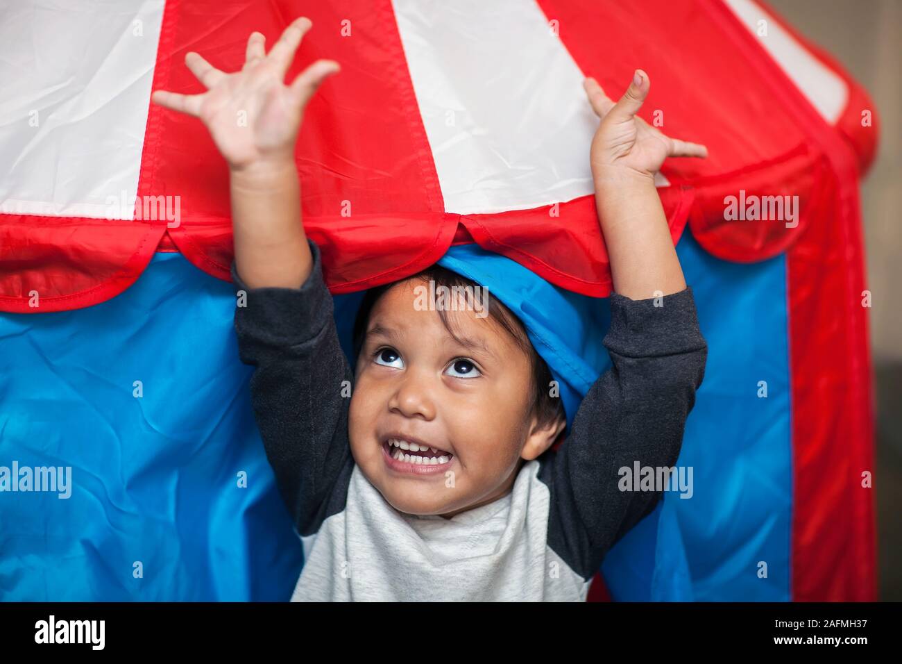 Un entusiasta giovane ragazzo saltando per la gioia che è rivolto verso il cielo come egli esce un rosso bianco e blu tenda play. Foto Stock