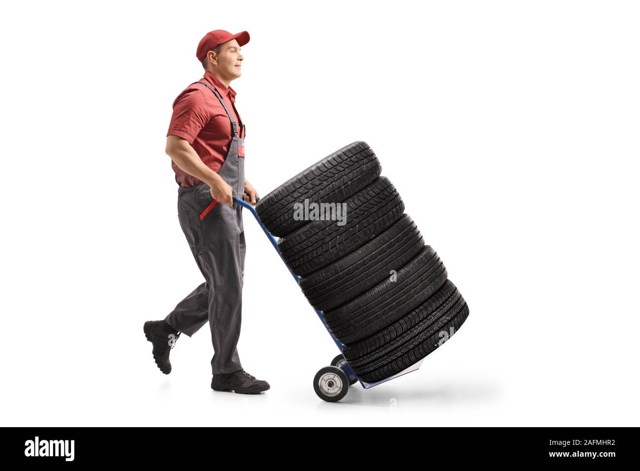 Lunghezza piena ripresa di profilo di un lavoratore spingendo gli pneumatici per auto con un carrello di isolati su sfondo bianco Foto Stock