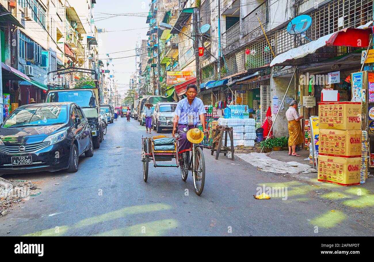YANGON, MYANMAR - 17 febbraio 2018: La scena urbana a Chinatown con macchine parcheggiate e risciò, equitazione lungo la meschina edifici, il 17 febbraio nella Foto Stock