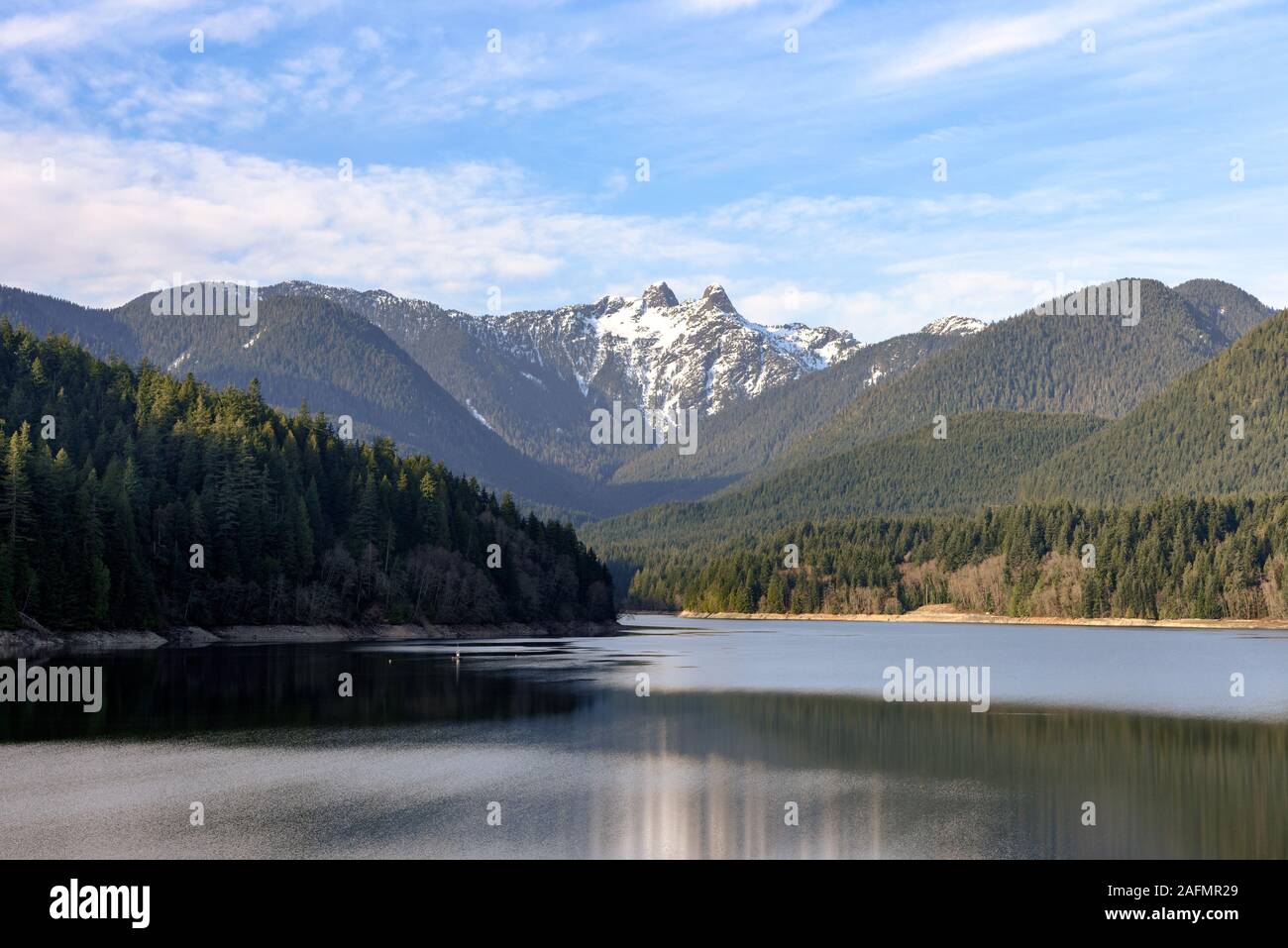 Il Capilano lago con le cime innevate vette Lions a distanza Foto Stock