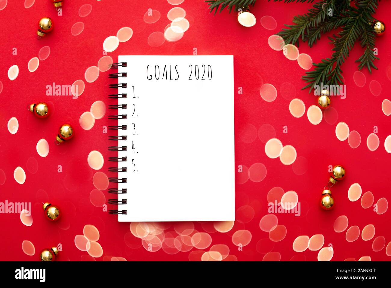 Notebook con 2020 degli obiettivi su sfondo rosso con golden decorazioni natalizie e verde abete il brunch. Vista dall'alto. Bokeh luci. Foto Stock