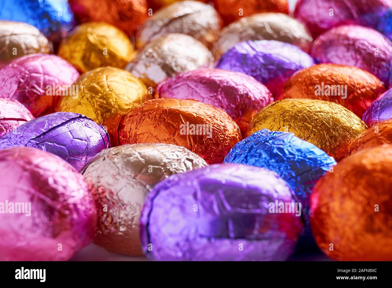 Molte uova di pasqua di cioccolato avvolto in blu, viola, arancione, rosa e lamina dorata wrap Foto Stock