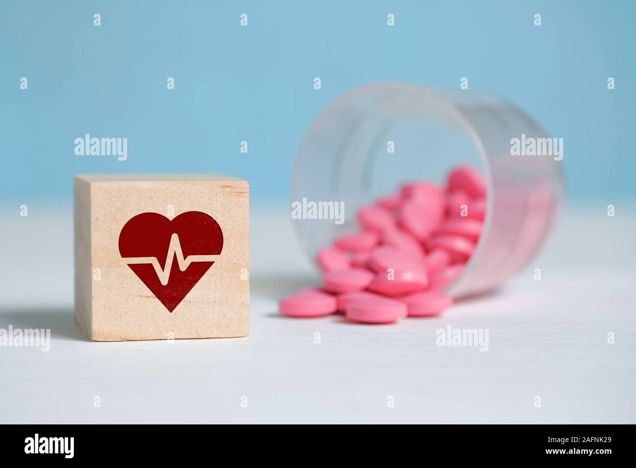 Il concetto di una dose giornaliera di farmaci per il cuore. Icona su una  piazza di legno accanto a compresse realizzato in una tazza di plastica.  Close up Foto stock - Alamy
