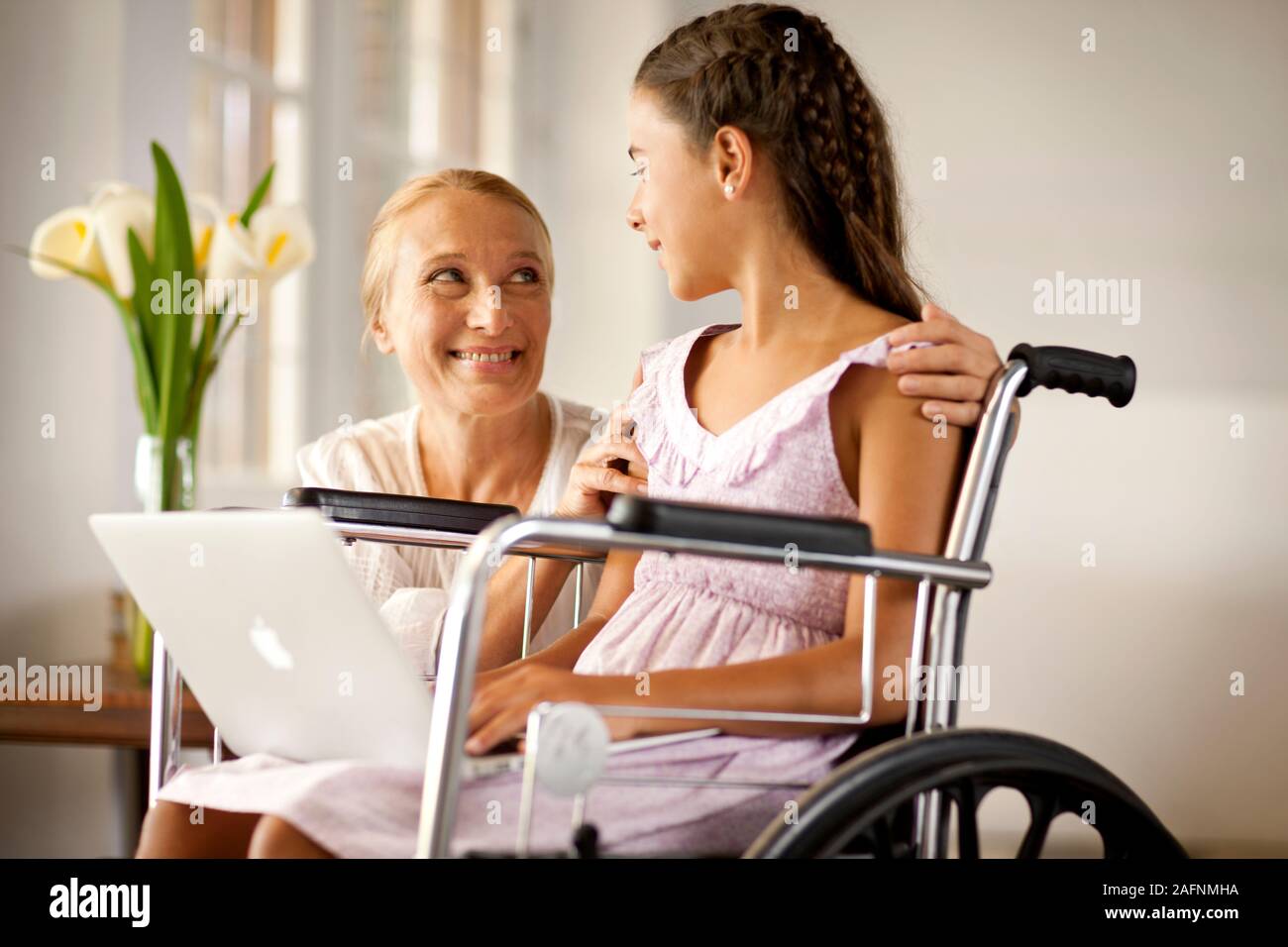 Donna matura inginocchiato accanto al suo nipote che è seduto nella sedia a rotelle. Foto Stock
