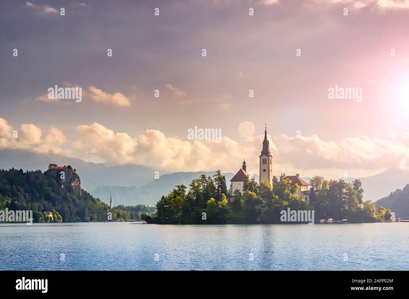 Incredibile tramonto sul lago di Bled, Slovenia con alte montagne e nuvole sullo sfondo. Chiesa di pellegrinaggio dell Assunzione di Maria, Castello di Bled. Il pos Foto Stock