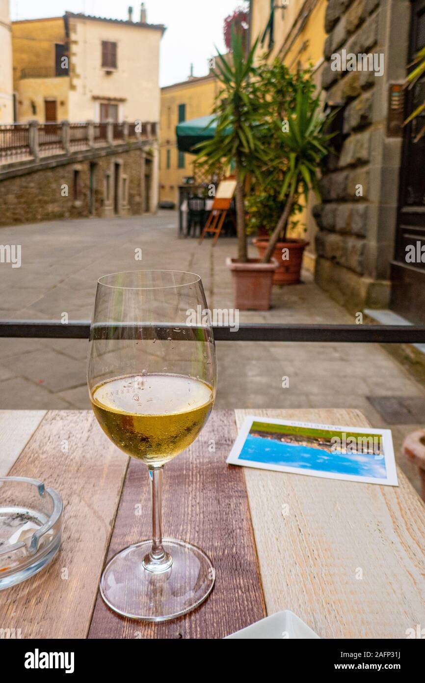 Un bicchiere di vino bianco con una cartolina su una tabella in una tipica strada italiana Foto Stock