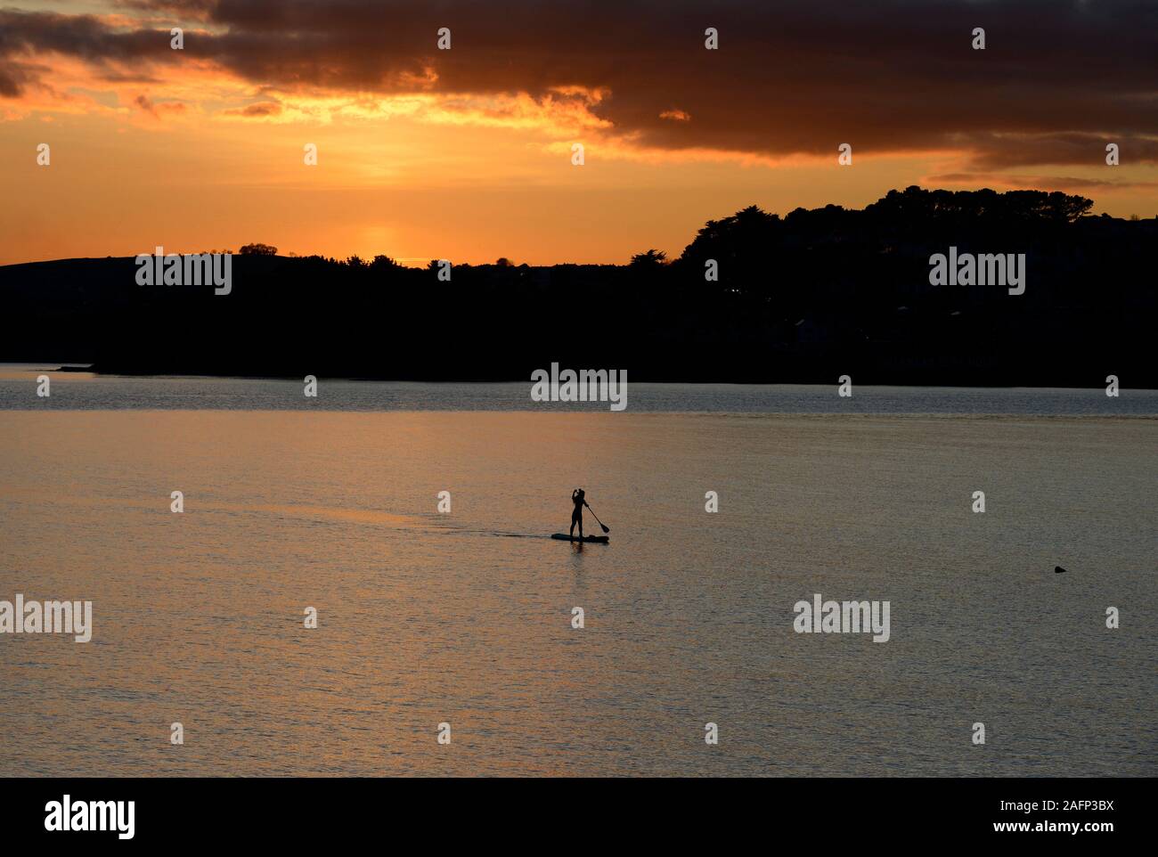 Un unico stand-up paddleboarder si avvicina al porto di Torquay in Devon in una giornata di mare calmo come il sole tramonta dietro di lei Foto Stock