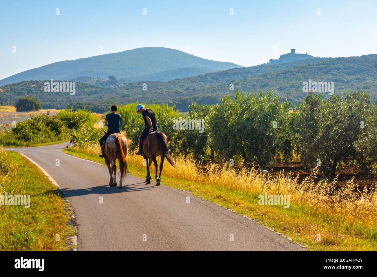 Due cavalieri su due cavalli con la skyline della città di Capalbio su sfondo in Toscana Italia Foto Stock