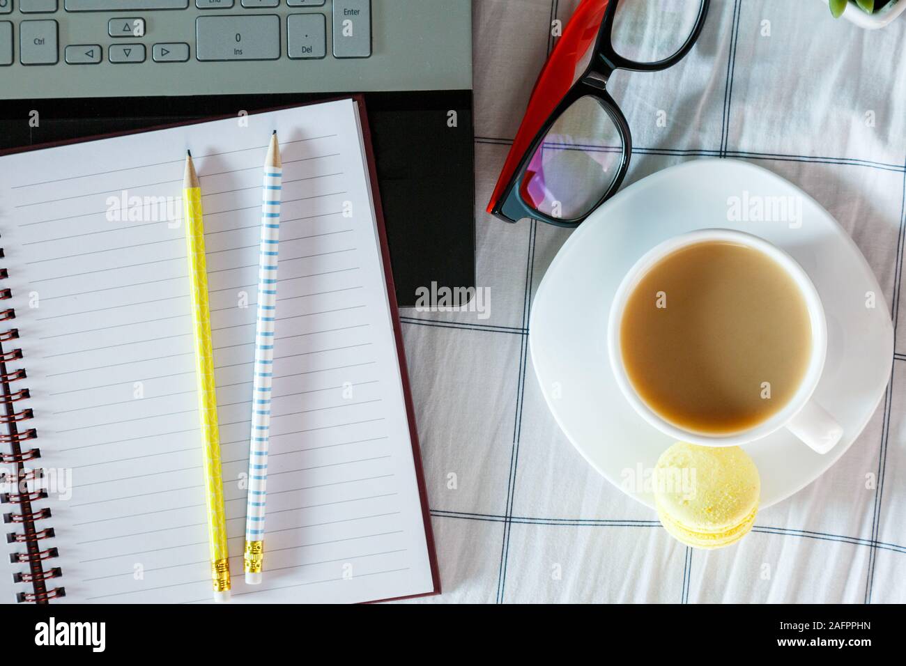 Close up sveglia rossa, matite, un notebook e una tazza di caffè nel letto. Area di lavoro per freelance. Ora di scadenza del concetto. Lay piatto Foto Stock