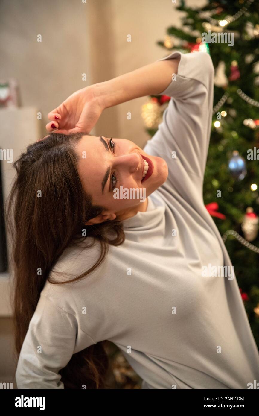 Felice giovane donna di fronte a albero di Natale di pensare e ridere Foto Stock