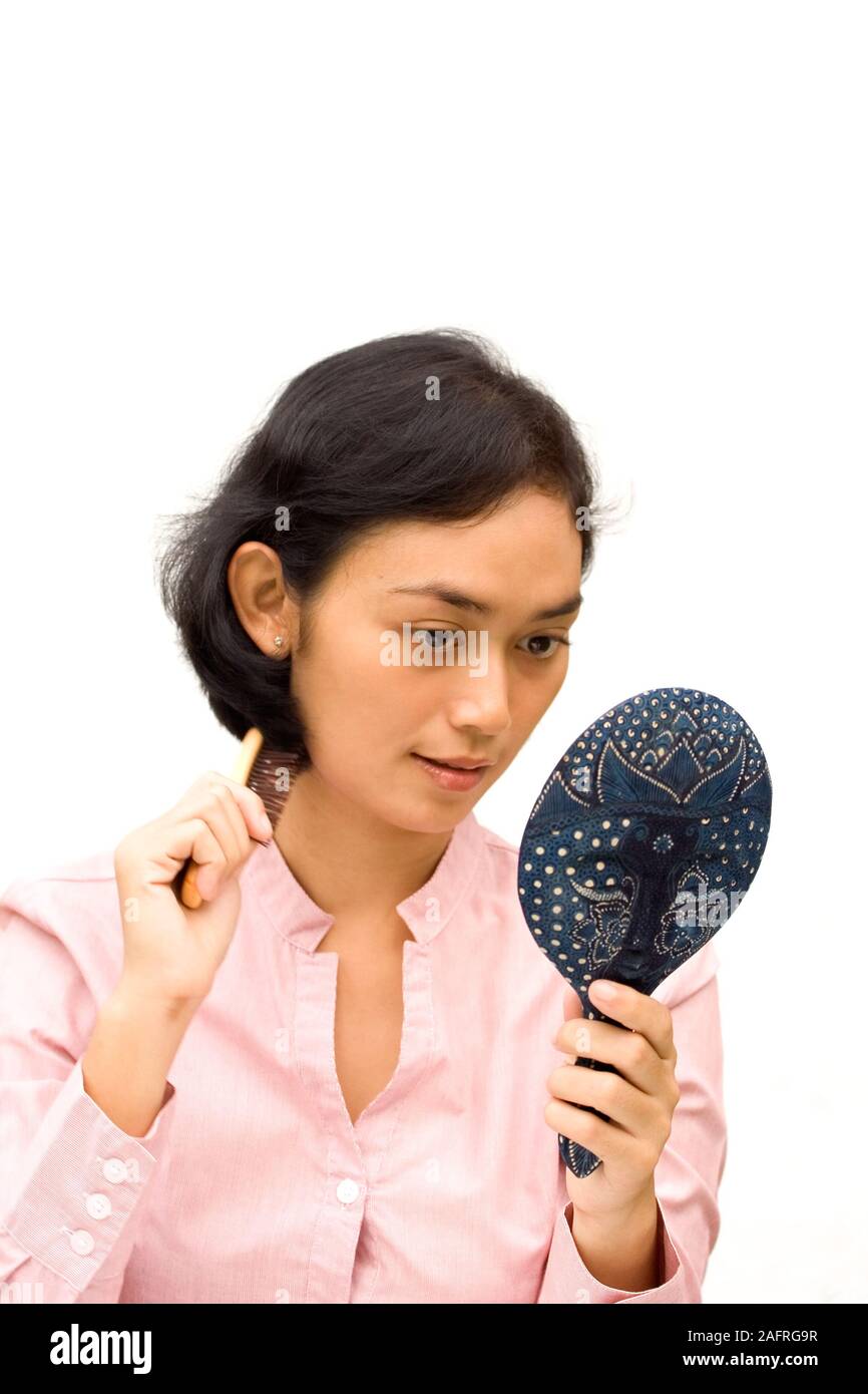 Sud-est asiatico giovane donna toelettatura con spazzola per capelli e lo specchio su mani isolato su bianco. Foto Stock