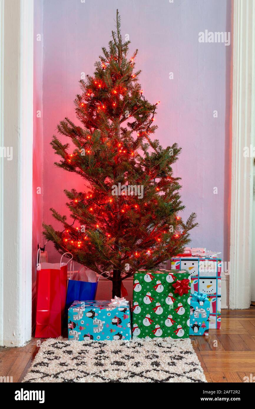 Piccolo albero di Natale decorato con luci rosse con regali e. Borse regalo sotto di esso in un soggiorno dell'appartamento Foto Stock