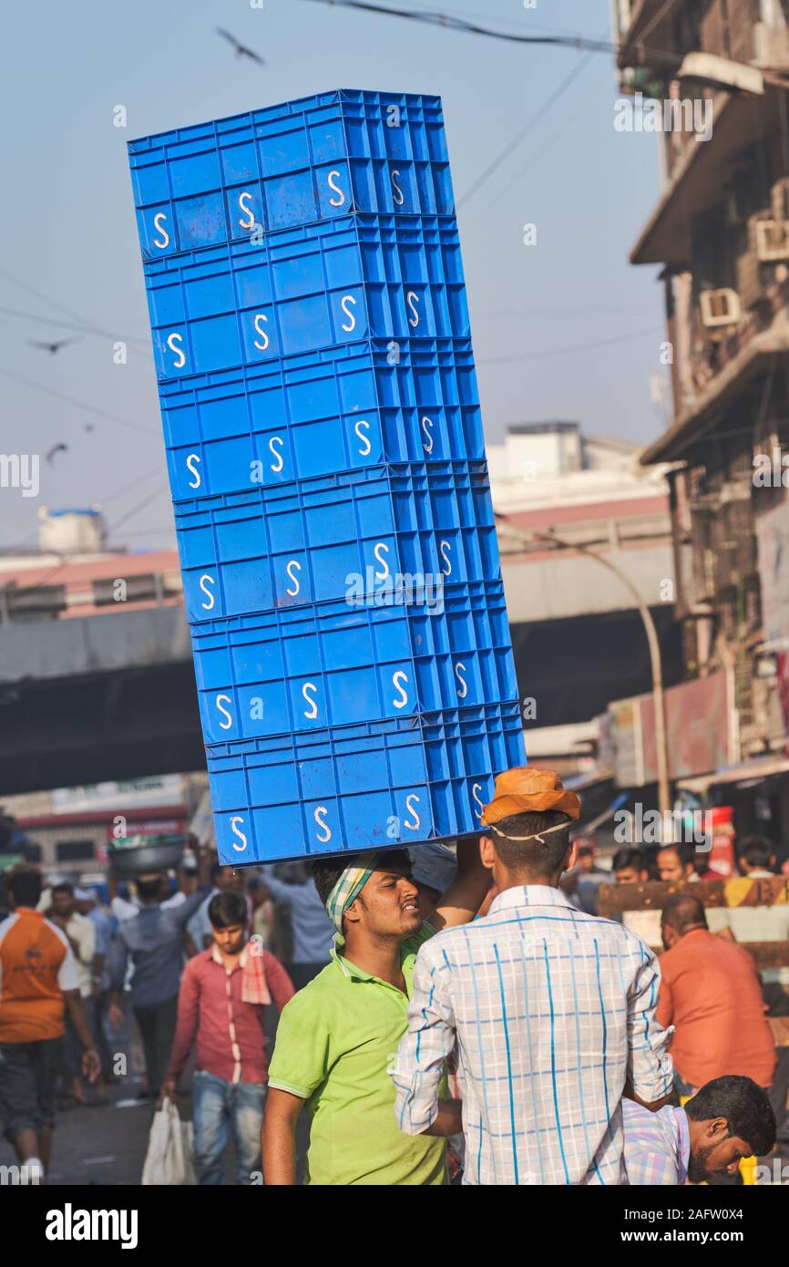 Un uomo che lavora in un mercato del pesce accanto al mercato Crawford in Mumbai (Bombay), India, saldi una mezza dozzina di cassette in plastica sulla sua testa Foto Stock
