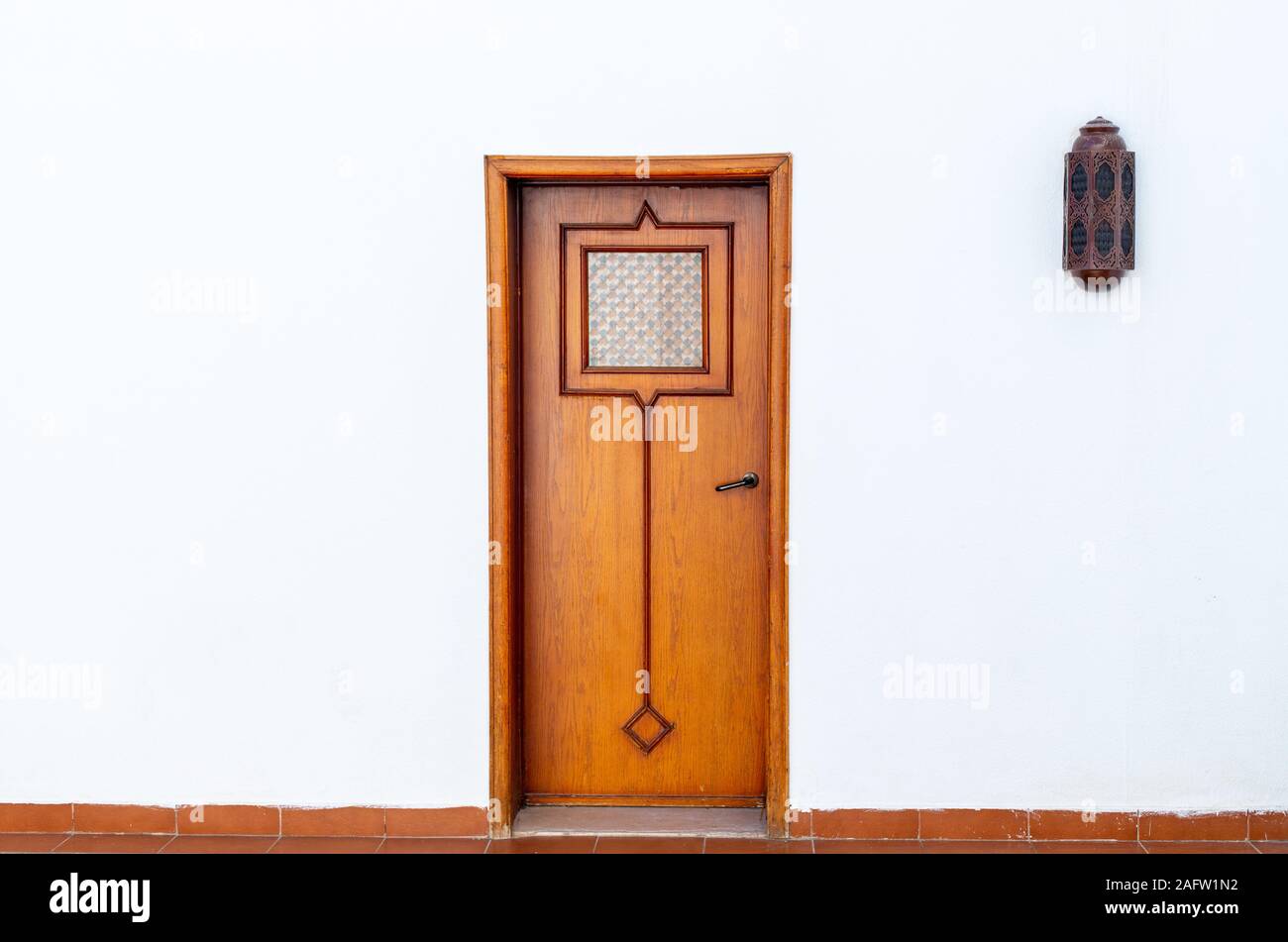 Vecchia porta in legno in stile arabo. Muro Bianco con una porta nel mezzo. Una lanterna sul lato su una parete bianca vicino alla porta. Il minimalismo concettuale. Foto Stock