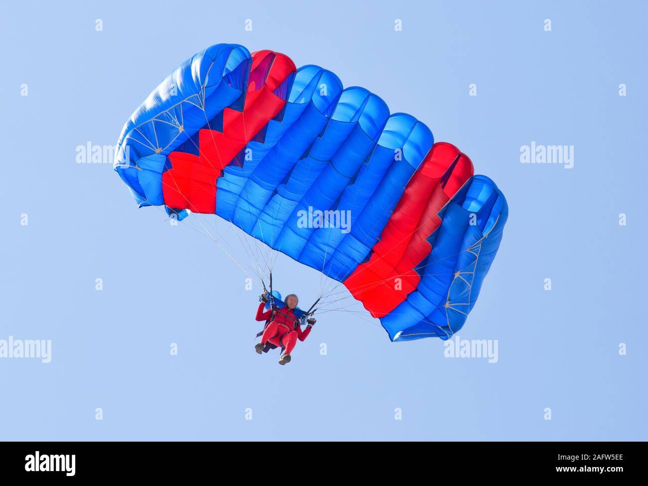 Paracadutista scende da paracadute nel cielo blu. La faccia è sfocata e irriconoscibile Foto Stock