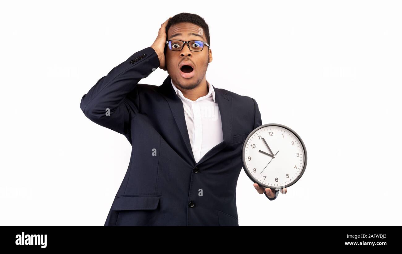 Scioccato afro guy holding orologio da parete su sfondo bianco Foto Stock