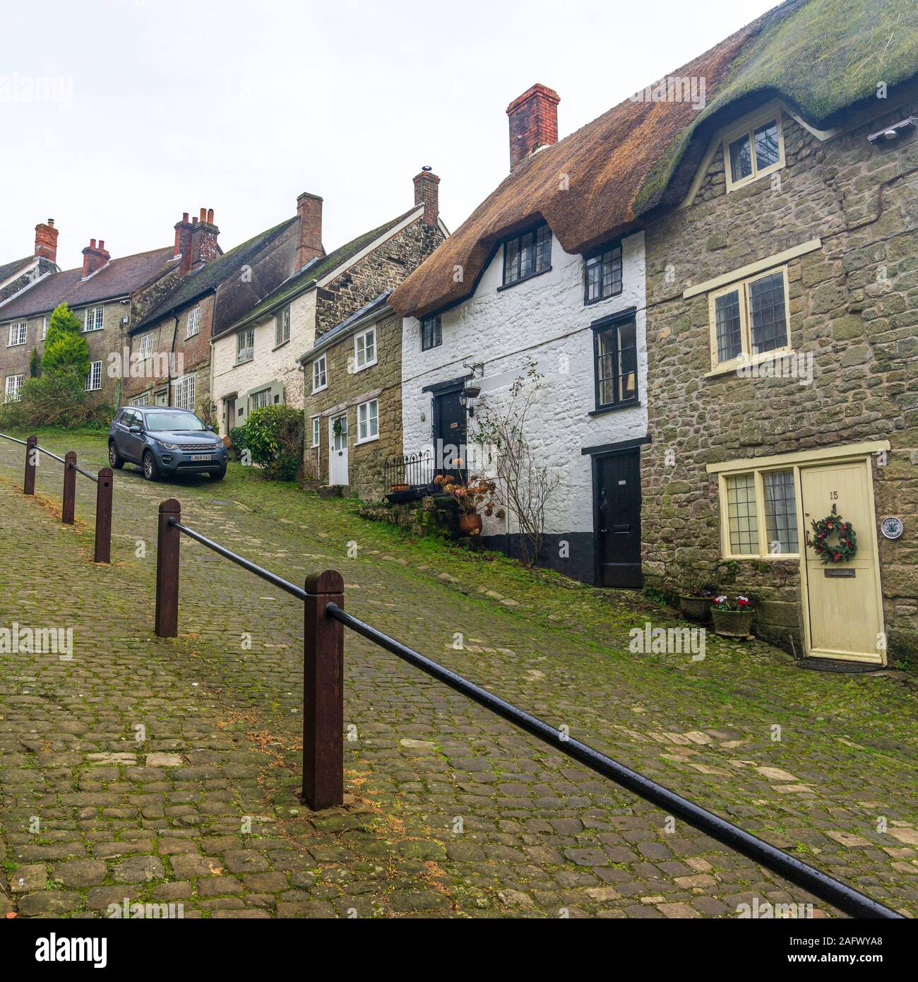 Auto parcheggiata sulla ripida strada di ciottoli con cottage con il tetto di paglia, Gold Hill, Shaftesbury, Dorset, Regno Unito nel mese di dicembre Foto Stock