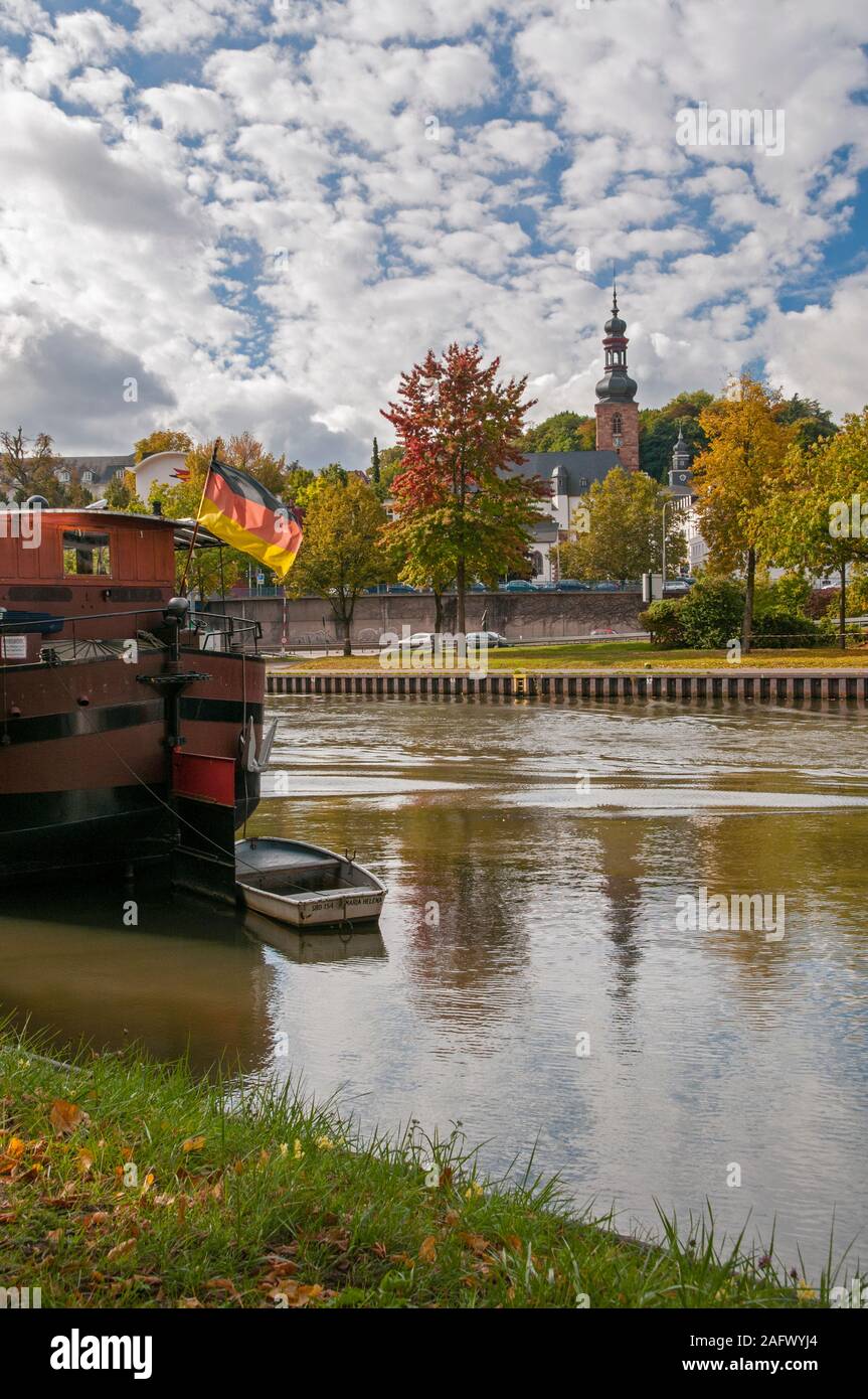 Le barche sul fiume Saar con una bandiera tedesca e la chiesa Schlosskirche in background, Saarbrucken, Saarland, Germania Foto Stock
