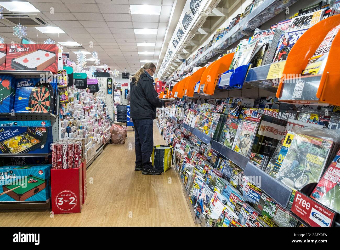 Un cliente shopper navigando attraverso la vasta selezione di riviste e periodici in vendita in un WH Smith shop store. Foto Stock