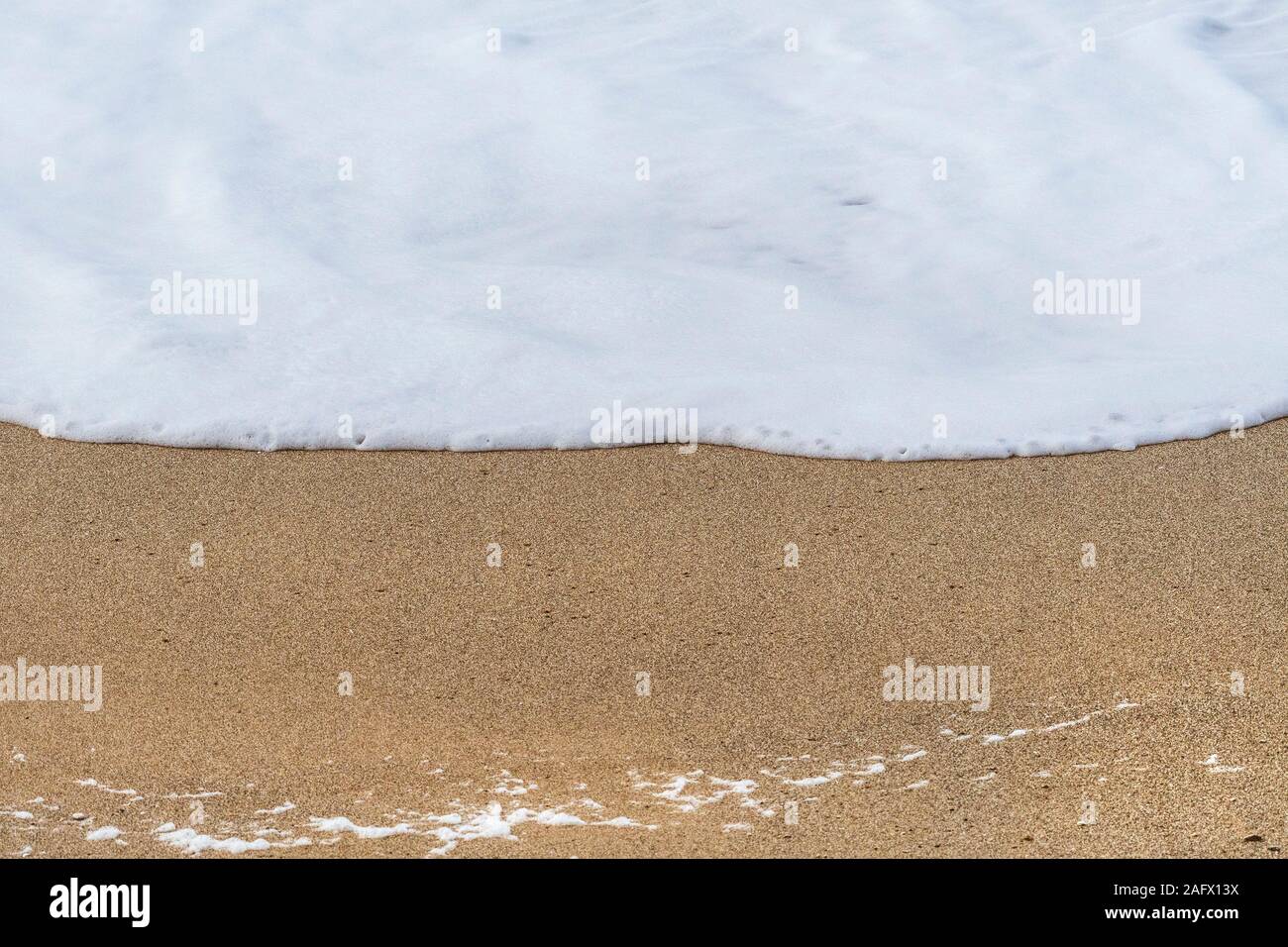 La schiuma di una piccola onda come esso scorre dolcemente fino a spiaggia. Foto Stock