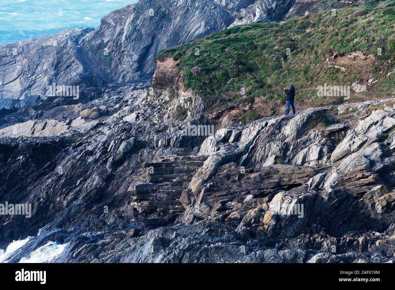Un uomo prendendo fotografie dalle rocce sul robusto e pericoloso costa a Towan testa in Newquay in Cornovaglia. Foto Stock