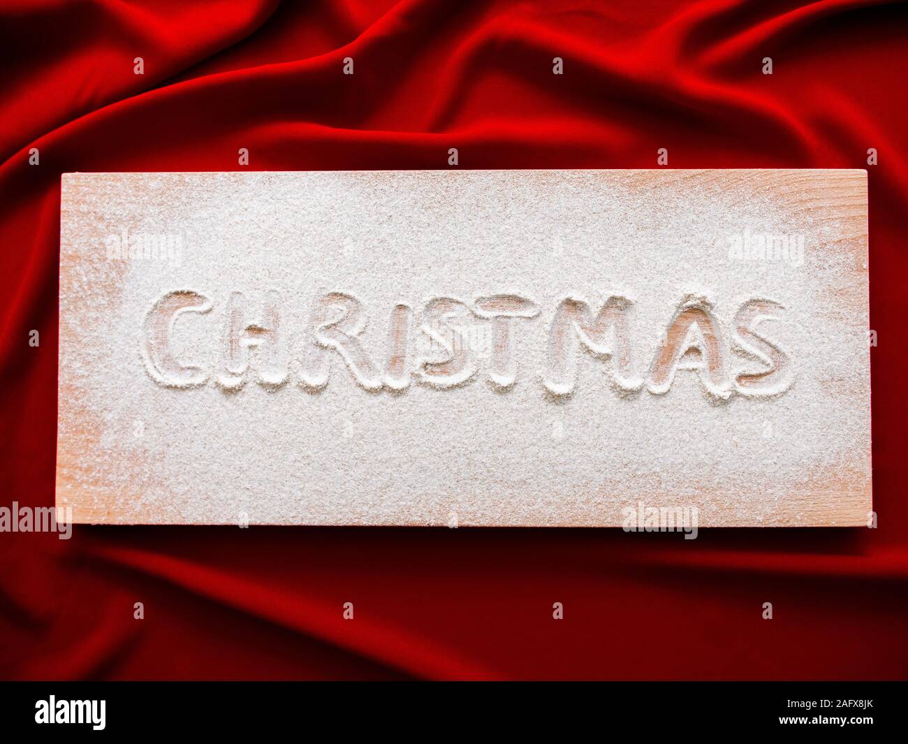 Buon Natale scritta su una tavola di legno Natale sfondo, vista dall'alto. Concetto baner card sul panno rosso Foto Stock