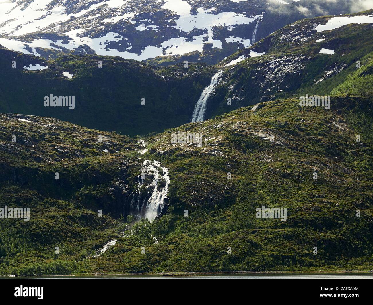 Nord del paesaggio con montagne e foreste in primo piano e il picco di montagna e cascata sullo sfondo. Senja Isola, Troms County, Norvegia. Foto Stock