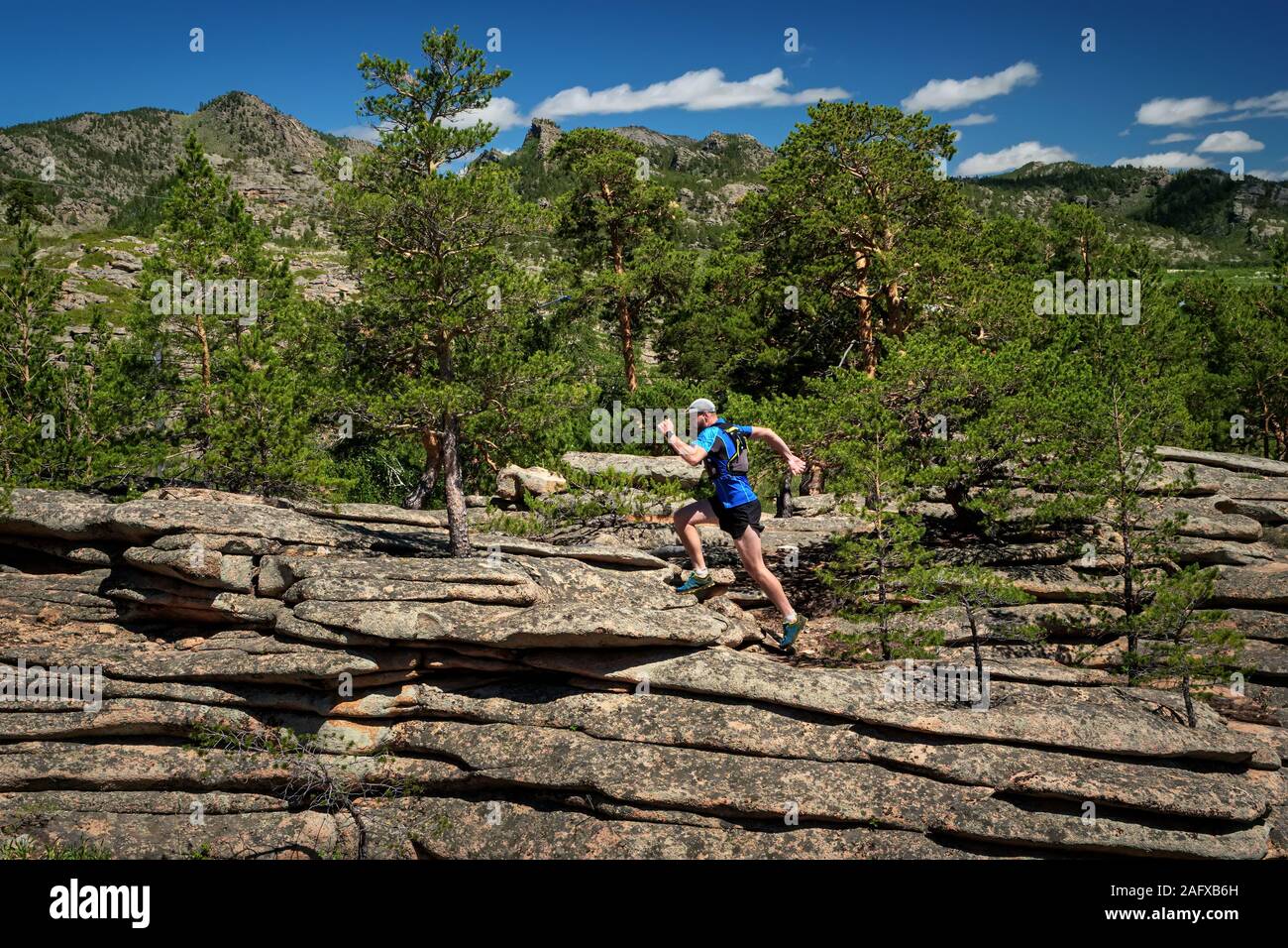 Runner arrampicata roccia. L'atleta corre sulle rocce in montagna. Outdoor trail running. Uomo in blu t-shirt e pantaloncini neri della formazione Foto Stock