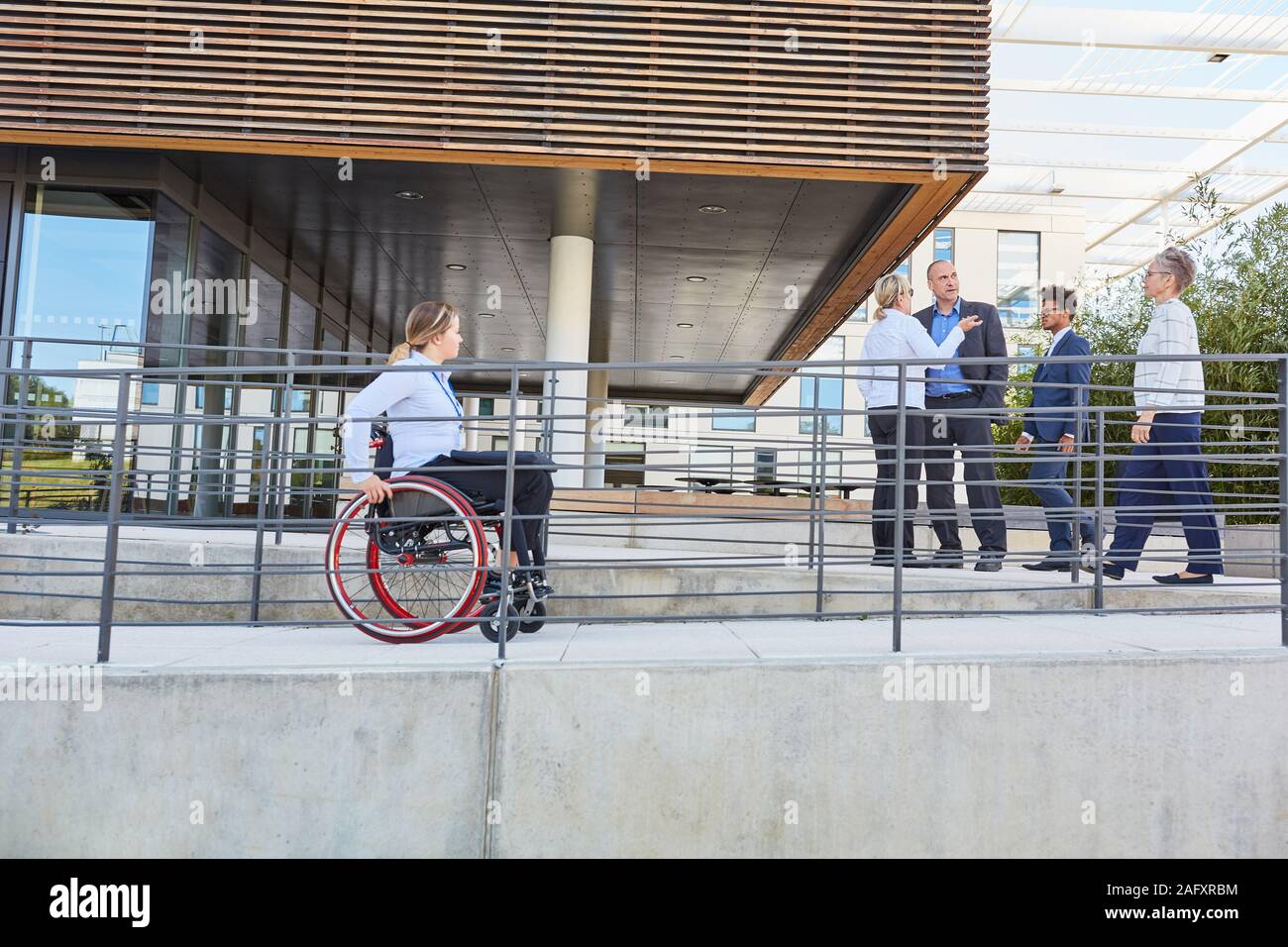 Donna disabile su sedia a rotelle rigidi fino alla rampa di un ufficio Foto Stock