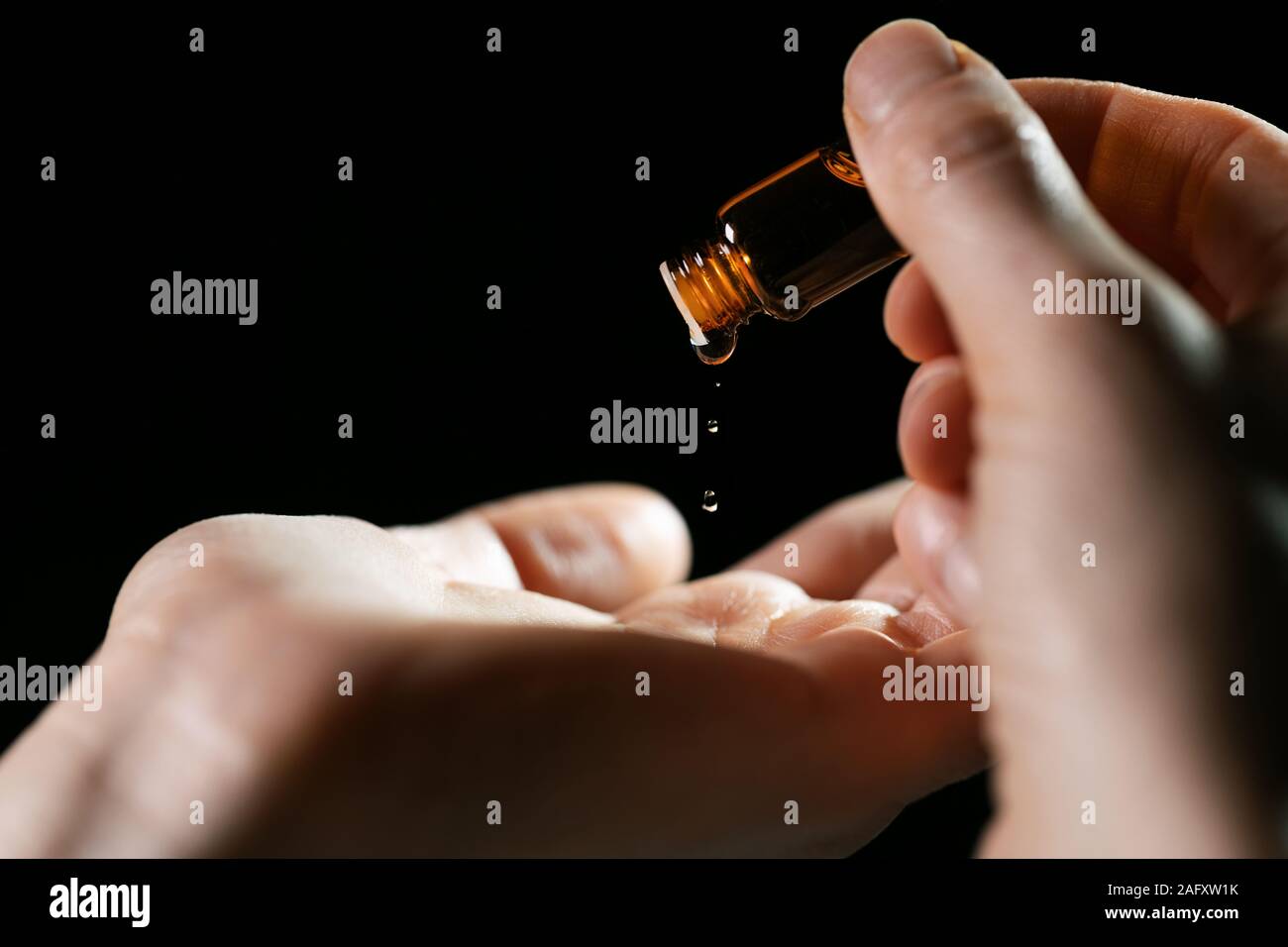 La cura della pelle e il trattamento - donna versando olio in una mano dal flaconcino su sfondo nero Foto Stock