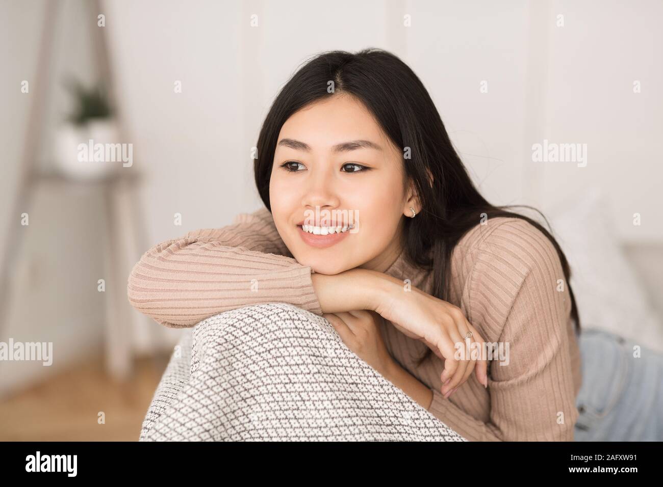 Carino ragazza asiatica in appoggio sul lettino a casa e sorridente Foto Stock