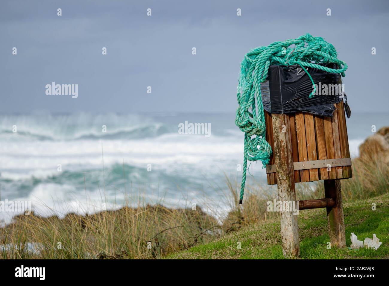 Coruna / Spagna - 15 dicembre 2019: verde aggrovigliati di corda in un cestino di legno può sulla cima di una scogliera che si affaccia sull'Oceano Atlantico Foto Stock