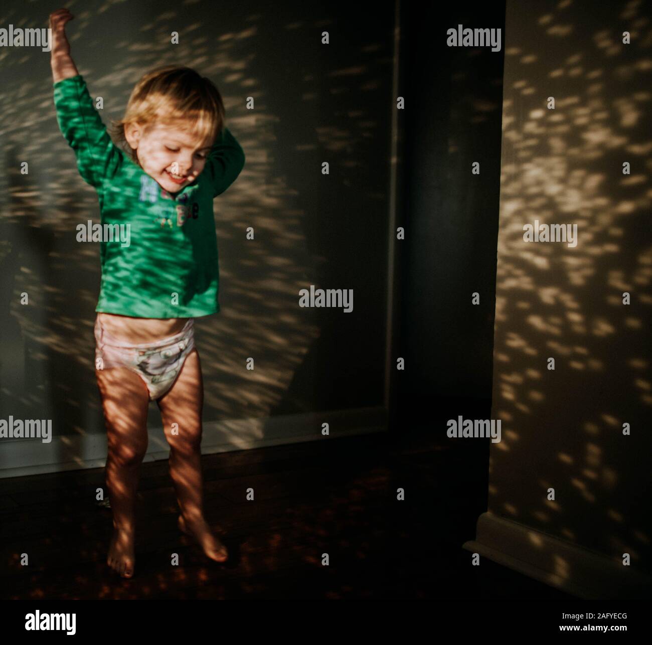 Il toddler stretching fino in riflessione della luce solare in corridoio Foto Stock