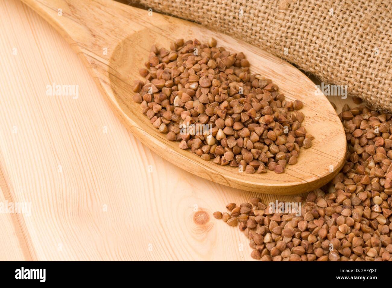 Il grano saraceno in un cucchiaio di legno. Sul tavolo di legno Foto Stock
