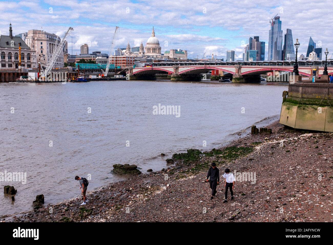La gente a piedi lungo il Tamigi come la marea è fuori, la Cattedrale di St Paul e la skyline di Londra dietro di loro, London, Regno Unito Foto Stock