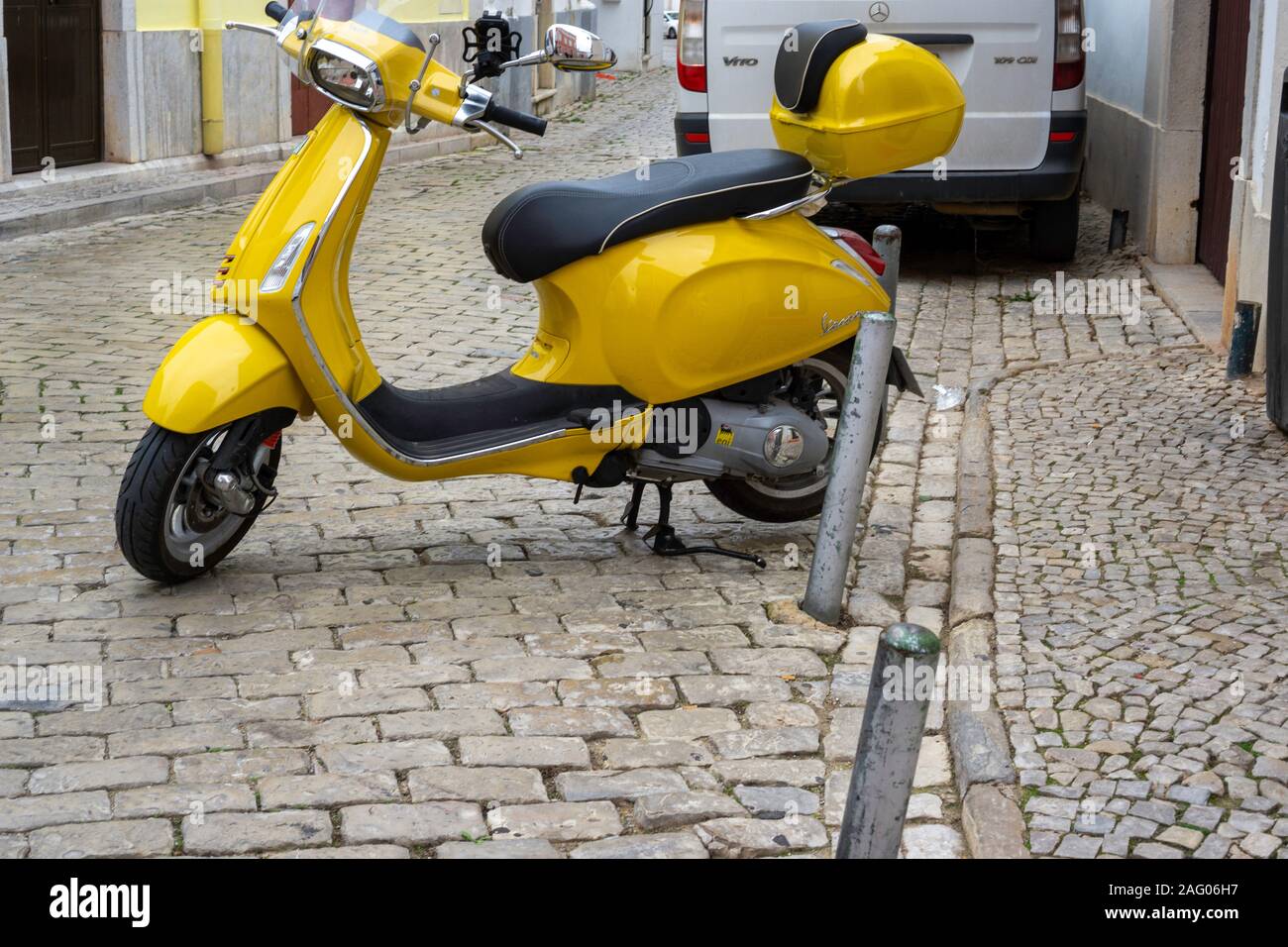 .Un giallo Vespa scooter parcheggiato su una mattonella lapidato road a Loulé, Portogallo Foto Stock