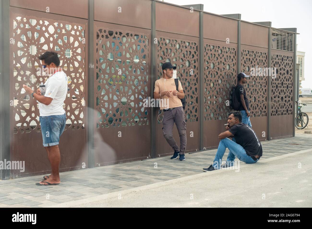 Quattro adulti in attesa per il bus dietro il bus shelter in città Khalifa, Abu Dhabi, Emirati arabi uniti Foto Stock