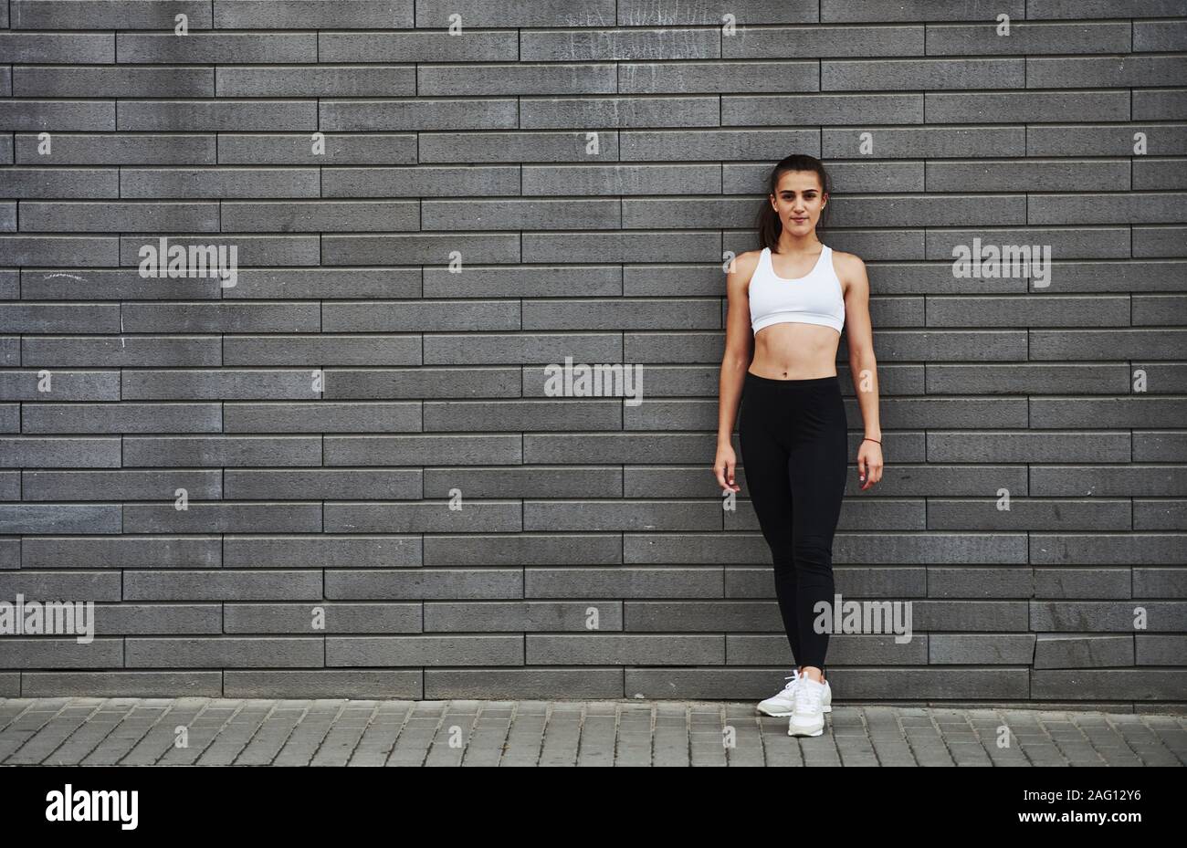 I giovani sportivi brunette con corpo sottile forma contro un muro di mattoni nella città di giorno Foto Stock