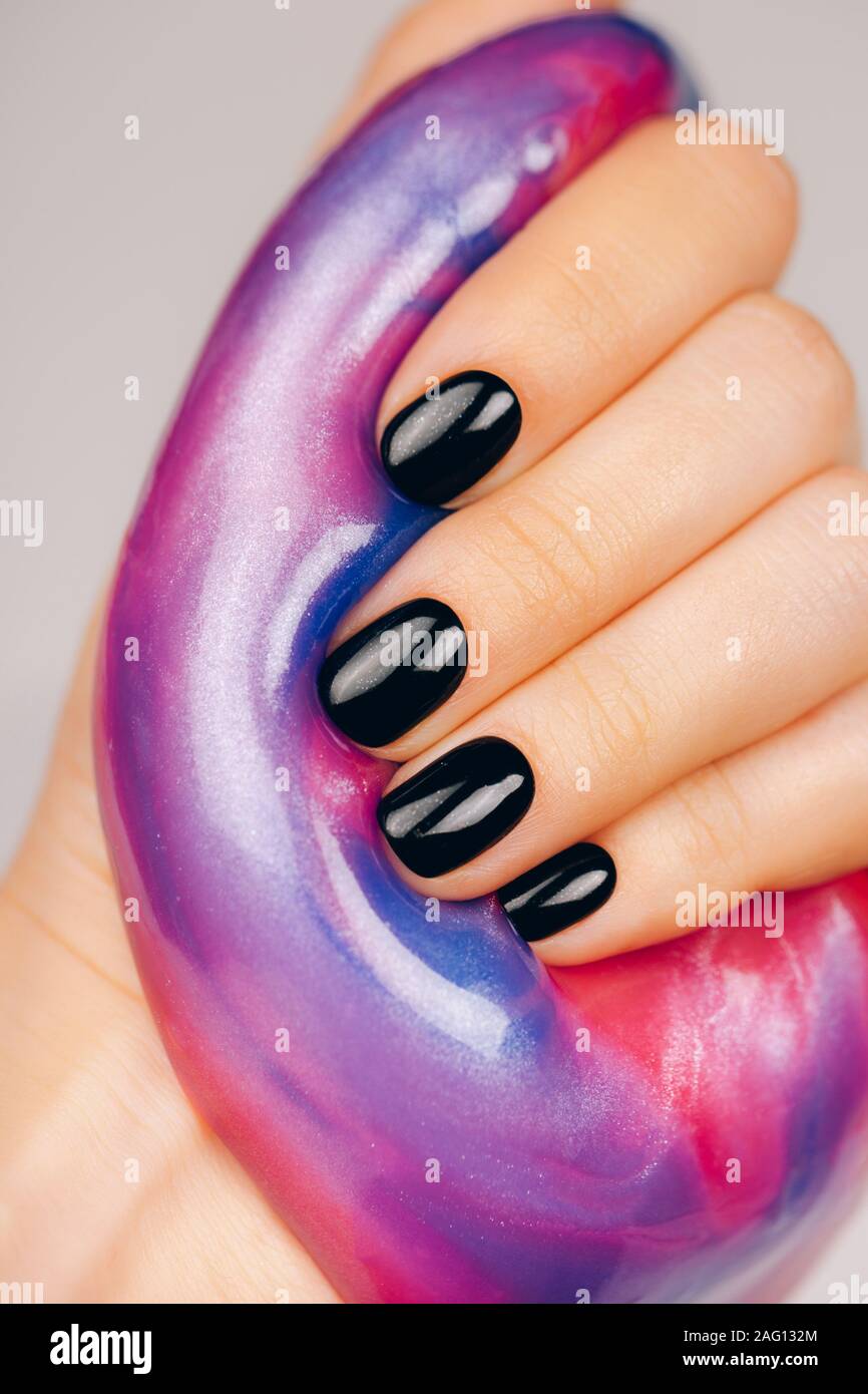 Mani con manicure nero tenendo il fango in blu e rosa colori vibranti Foto Stock