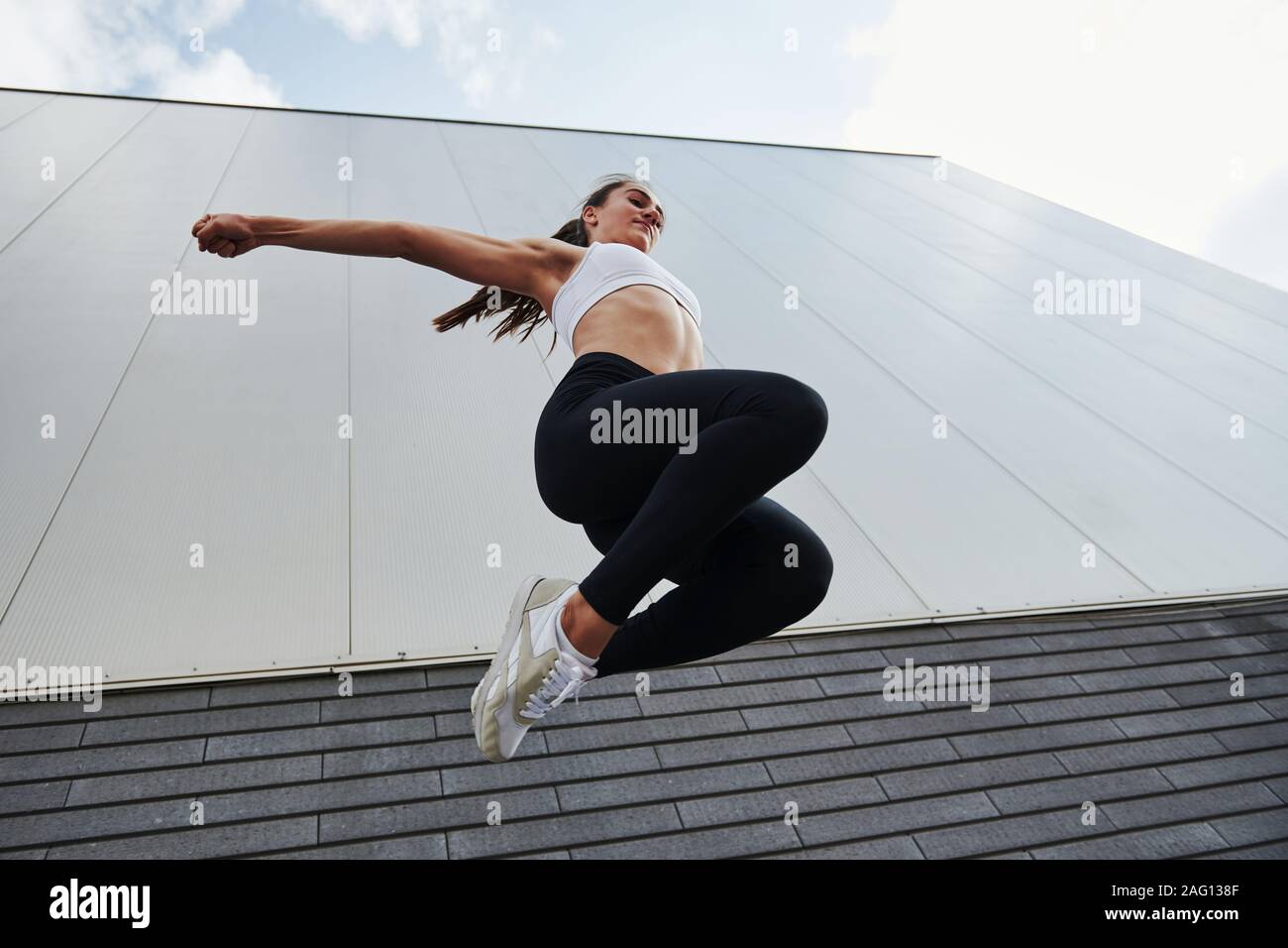 Vista dal basso. Giovani sportive fare parkour in città al giorno soleggiato Foto Stock