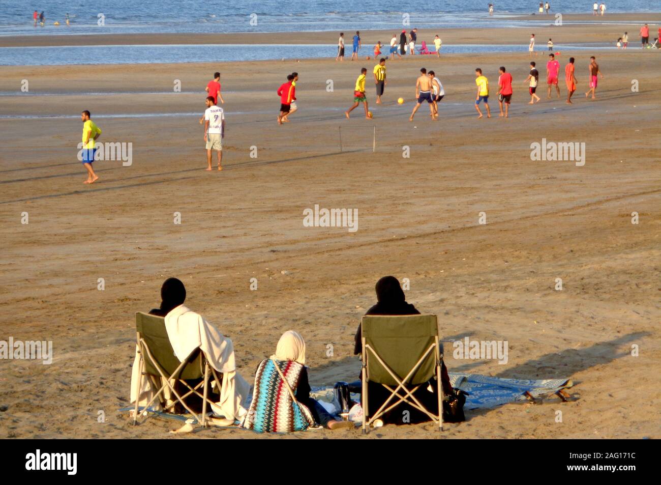 Omani donne guardare gli uomini giocare a calcio su una spiaggia in Muscat Oman Foto Stock