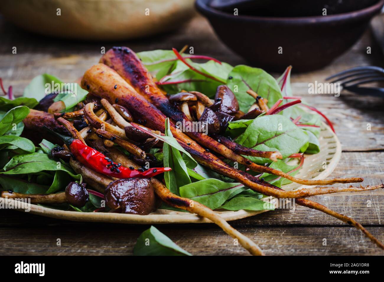 Impianto basato cibo, arrosto di Prezzemolo a grossa radice con funghi e bimbo fresche foglie di bietole in ciotola ceramoc su tavola in legno rustico Foto Stock