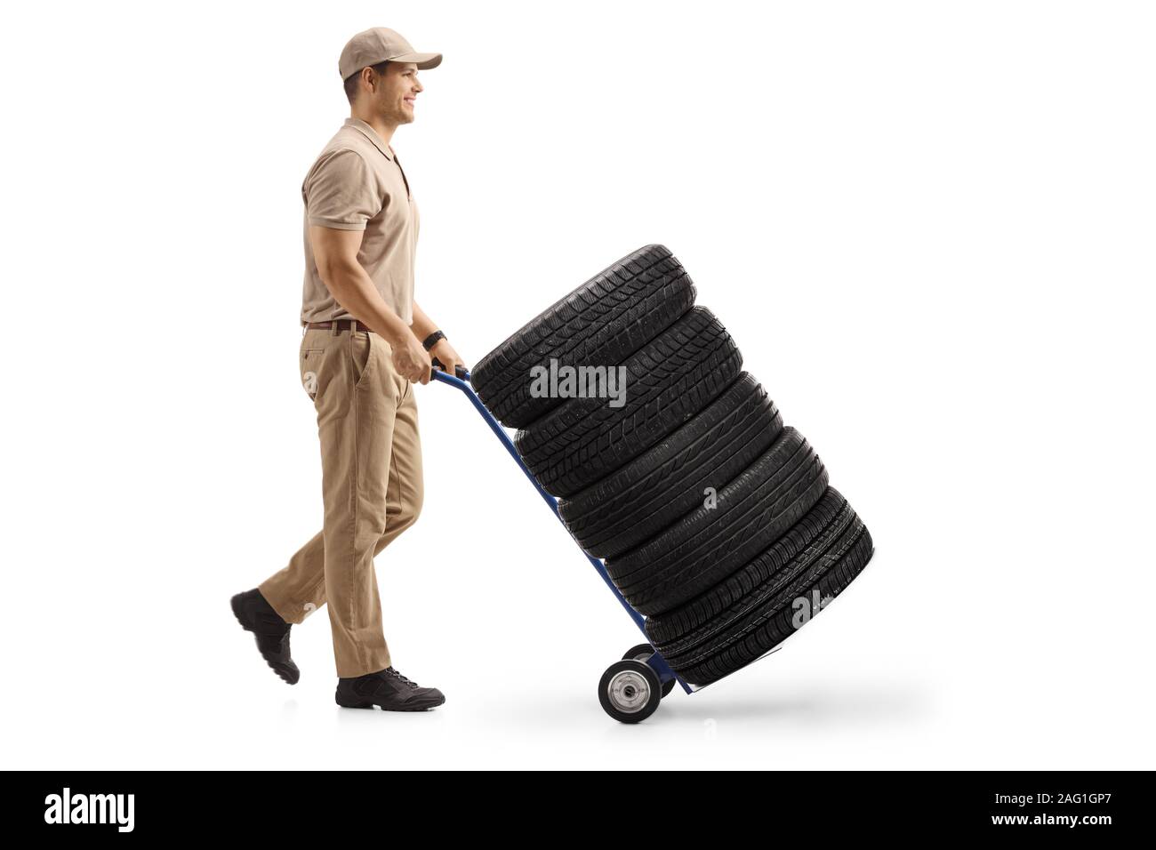 Lunghezza piena ripresa di profilo di un uomo di consegna spingendo un carrello caricato con gli pneumatici per auto isolati su sfondo bianco Foto Stock