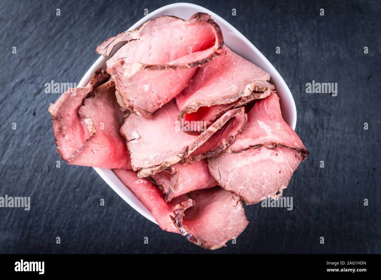 Porzione di Roastbeef (tagliata a fette; messa a fuoco selettiva) su una lastra di ardesia Foto Stock
