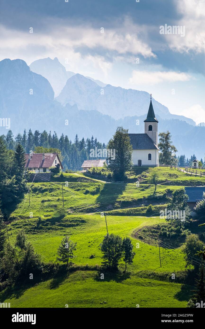 Chiesa Cerkev Sveti Duh in Solčava con mountain range Kamnik-Savinja Alpi in Slovenia su una soleggiata giornata estiva Foto Stock