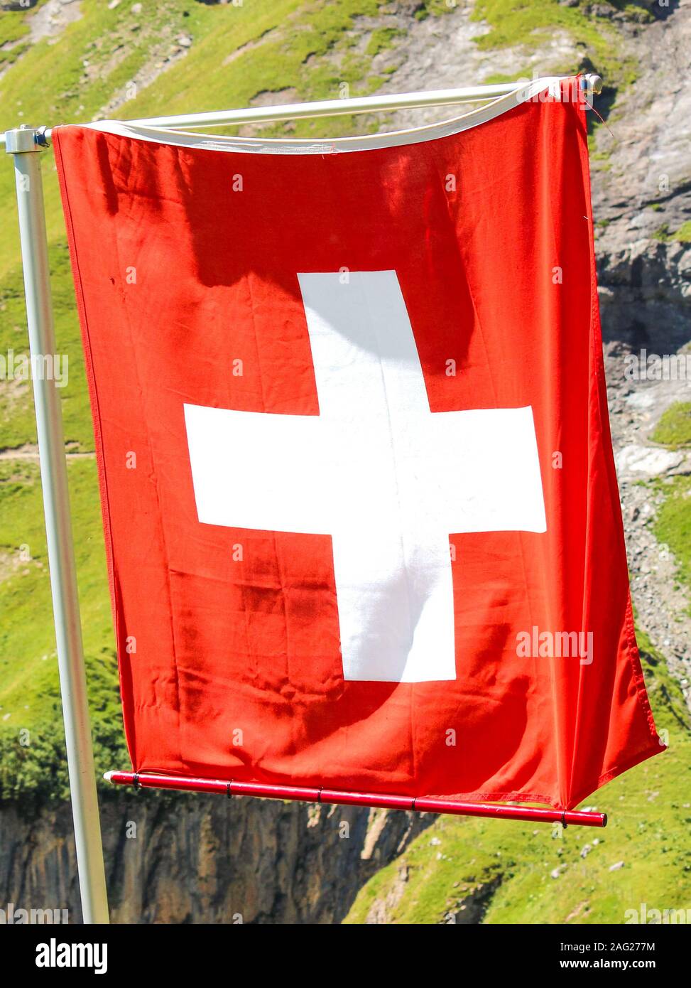 Sventola bandiera nazionale della Svizzera con sfocate paesaggio alpino in background. La croce bianca in un quadrato rosso. Simbolo nazionale del paese europeo. Bandiera svizzera su una foto verticale. Foto Stock