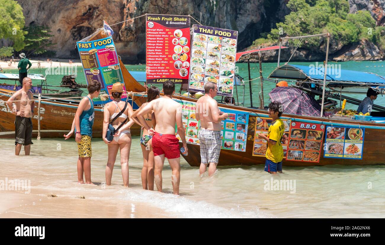 Railay, Krabi / Tailandia - Luglio 14, 2019: un gruppo di turisti si erge in mare surf e orologi menu di un ristorante in barca a Phranang Cave Beach. Foto Stock