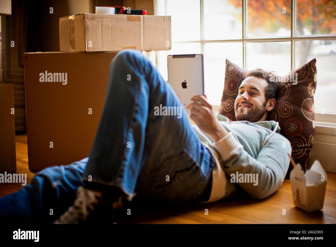 Metà di uomo adulto che giace sul piano della sua nuova casa e utilizzando il suo digitale compressa. Foto Stock